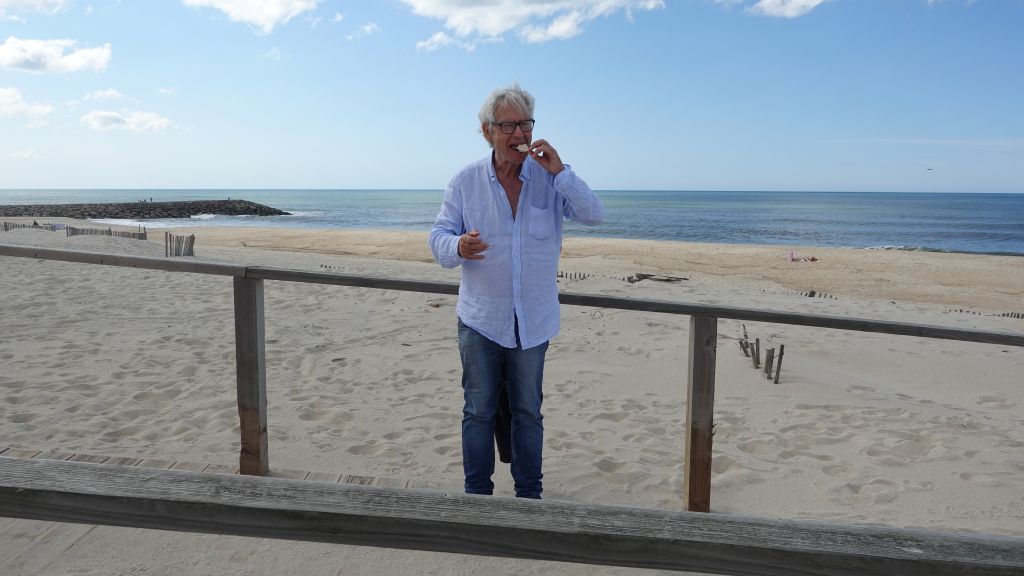 Die ehemaligen Fischerhäuser – Palheiros - das Fotomotiv in Costa Nova - Klaus verspeist einen Snack an der Promenade, im Hintergrund Strand und Meer